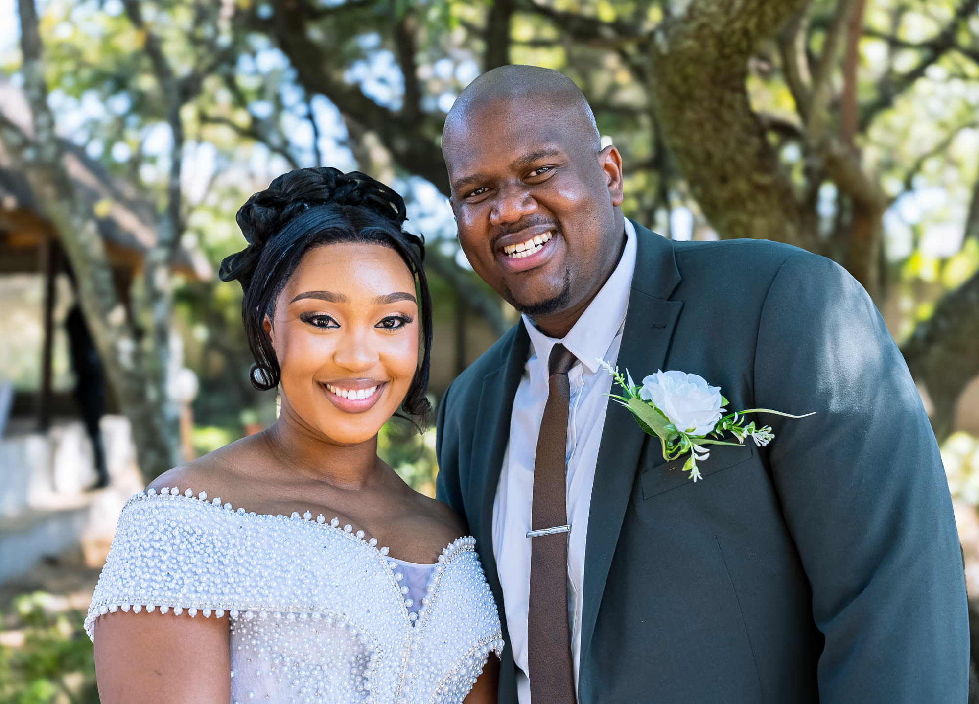 Close-up portrait of Musa in a dark green suit beside Chantal in her pearl-beaded gown